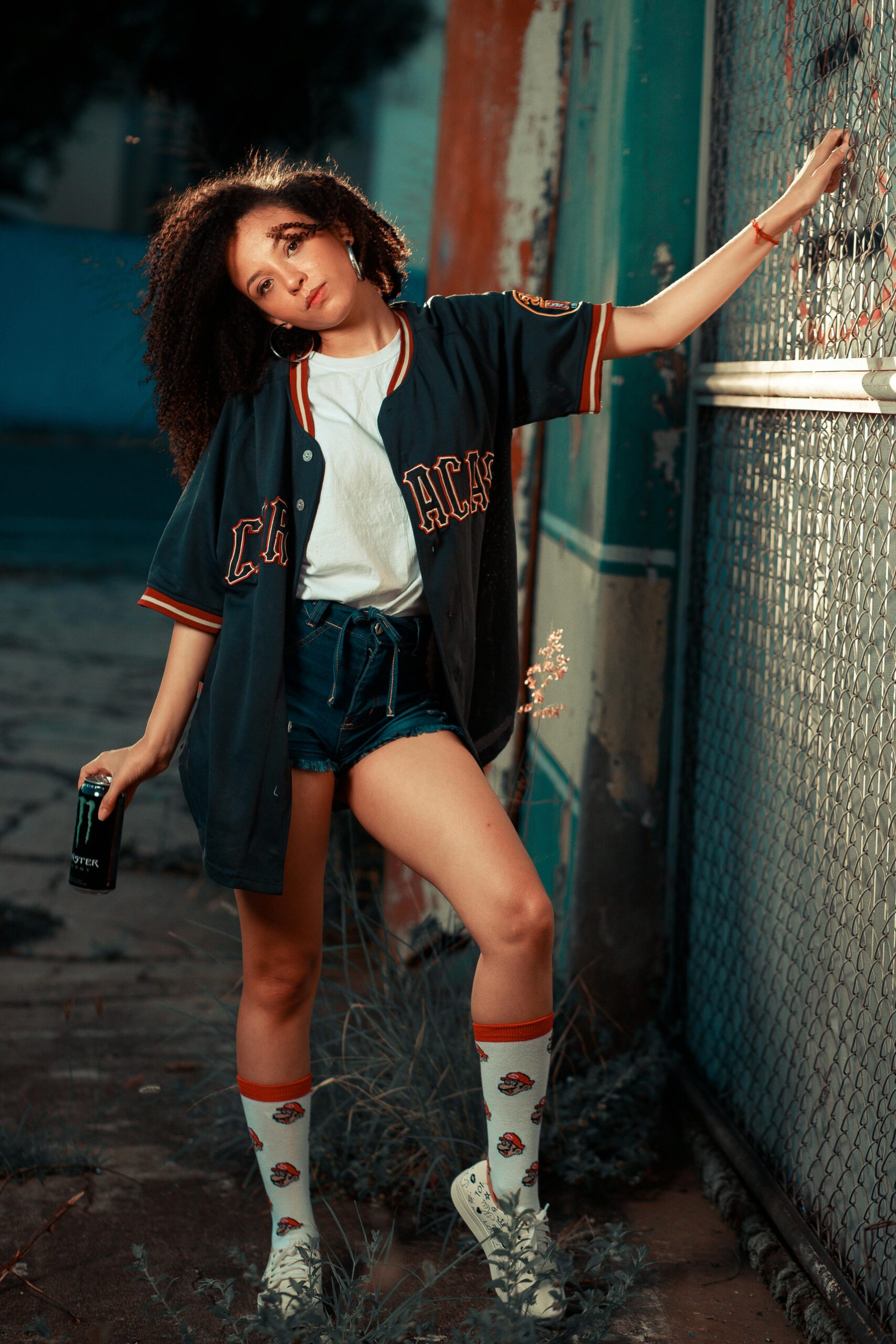 Teen girl in urban sportswear posing outdoors next to a graffiti wall at twilight.